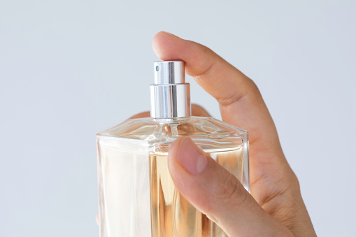 Unrecognizable woman showing perfume to camera in front of white background.