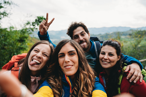 Four friends are taking a selfie during a trekking together. Pov view of friends looking at camera and making funny faces.