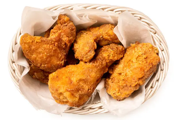 Crispy fried chicken pieces in a white woven basket isolated on white. Top view.