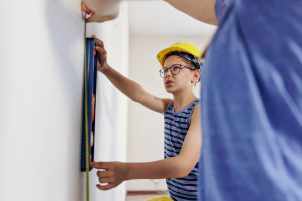 Teenage kids helping in house renovation. The kids are preparing for the painting. They are measuring the height of the painting area with tape measure.\nCanon R5