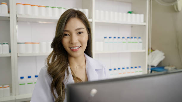 istock Smiling Asian pharmacist in drugstore or pharmacy using computer and looking at camera 1479736415