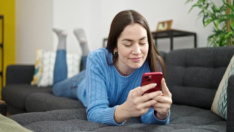 Young caucasian woman using smartphone lying on sofa at home