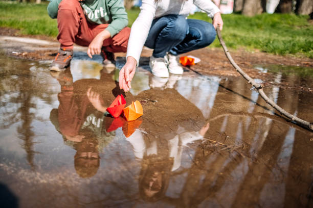 Boy playing with ship maid of paper floating on water puddle
