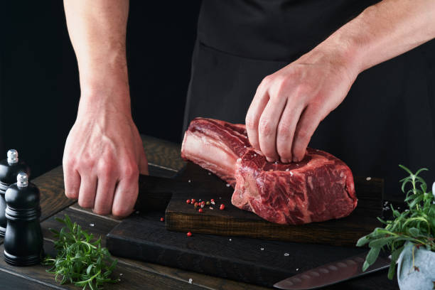istock Chef cutting steak beef. Mans hands hold raw steak Tomahawk on rustic wooden cutting board on black background. Cooking, recipes and eating concept. Selective focus. 1479741036