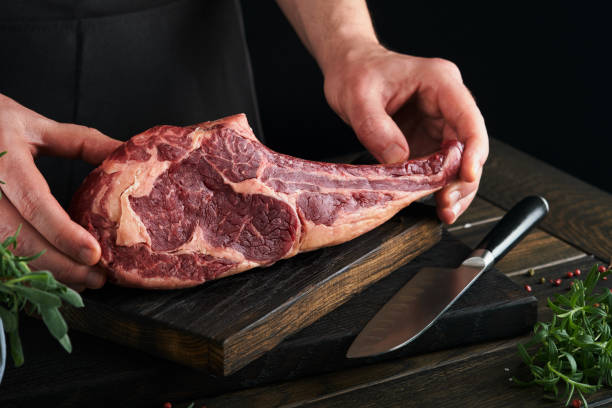 istock Chef cutting steak beef. Mans hands hold raw steak Tomahawk on rustic wooden cutting board on black background. Cooking, recipes and eating concept. Selective focus. 1479741073