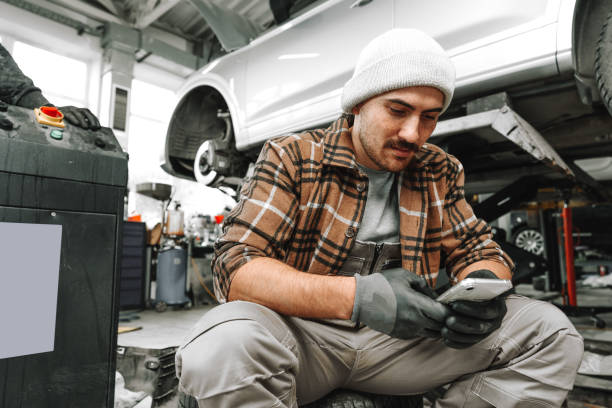 istock Car service worker sitting on a wheel and resting, using mobile phone 1479741370