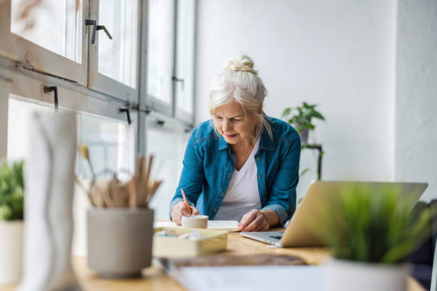 istock Smiling mature businesswoman writing in notebook while sitting at table in office 1479743039