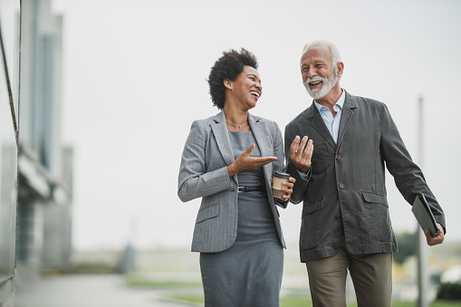 Shot of two successful multi-ethnic business people talking and having fun while walking during a coffee break outdoors.