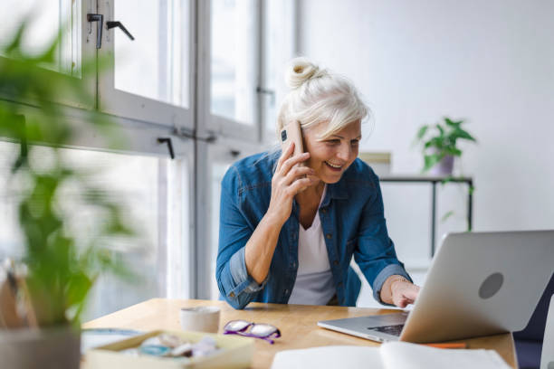 istock Smiling businesswoman talking on mobile phone while using laptop in office 1479743716