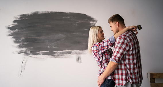 Home renovation and relationships concept. Loving couple hug near their freshly painted wall in room. Copy space. Banner