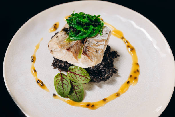 gebackener fisch auf einem reiskissen mit tintenfischtinte, garniert mit algen und papayasauce. - japanese cuisine appetizer gourmet caviar stock-fotos und bilder