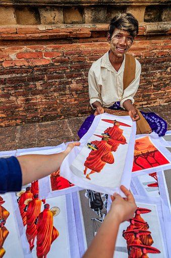 Young Burmese boy with thanaka face paint selling souvenirs - sand paintings, in the ancient temple of Bagan, Myanmar (Burma)