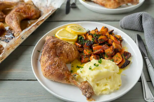 Homemade healthy and gluten free dinner or lunch with oven baked or roasted chicken legs. Served with roasted and marinated pumpkin salad and mashed potatoes on a plate.
