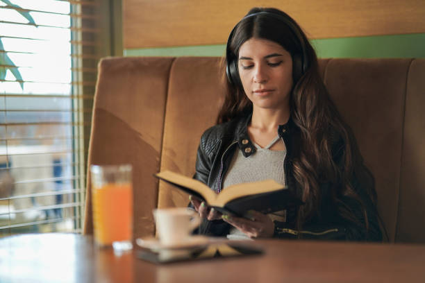Beautiful young woman relaxing listening to music and reading a book in a cafe.