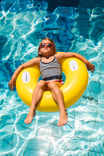 Little girl enjoys her vacation lying in inflatable ring into the swimming pool