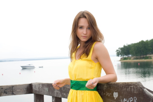 Beautiful young girl in a long yellow dress on a background of water