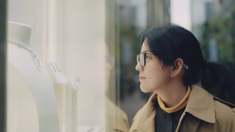 young asian woman with shopping bags picking jewelry in modern luxury shop, smiling