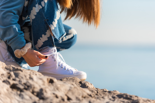Teenage Girl on a Sunny Winter Day at the Sea Shore Tying White Sneakers