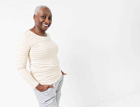 Portrait of an African American senior woman standing against a white background, hands in pocket