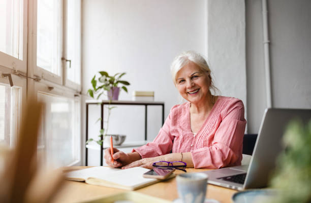 istock Smiling mature businesswoman writing in notebook while sitting at table in office 1479774747