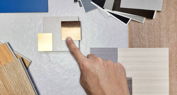 architect's hand choosing interior material samples contains travertine tile, gold stainless, roller blind drapery, wood vinyl floor tile, interior fabric wallpaper, quartz, laminated. close up view. la mano del arquitecto que elige las muestras de materiales interiores contiene baldosas de travertino, inoxidable dorado, cortinas enrollables, baldosas de vinilo de madera, papel tapiz de tela interior, cuarzo, laminado. vista de cerca.