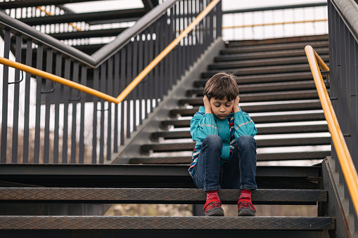 Boy covering his ears while sitting on stairs