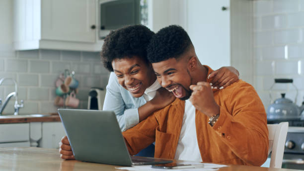 istock Couple Use Laptop Computer, Do High-Five in Celebration, while Sitting in their Apartment. Boyfriend and Girlfriend Talk, Shop on Internet, Choose Product to Order Online. 1479777920
