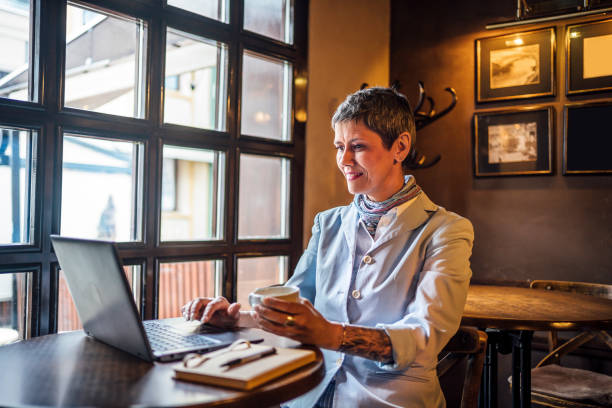 istock Mature woman using a laptop at the cafeteria while drinking coffee 1479778581
