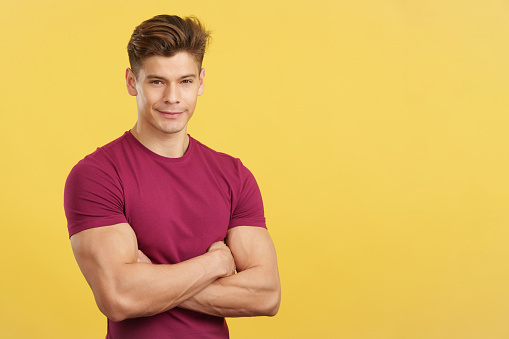 Strong man smiling at the camera with arms crossed in studio with yellow background