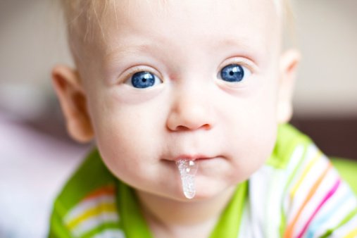 A closeup portrait of a blond blue-eyed baby having saliva dripping copiously from the mouth