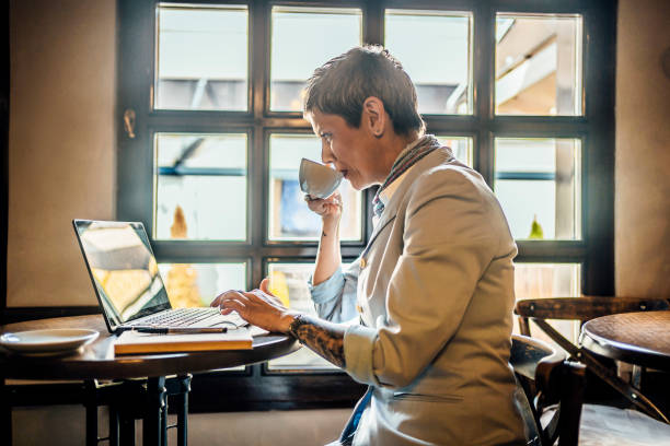 istock Mature woman using a laptop at the cafeteria while drinking coffee 1479780173