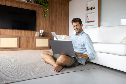 Happy Brazilian man paying his utility bills online at home - domestic life concept