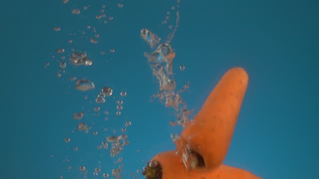 Slow motion fresh juicy orange carrot falls into the water.