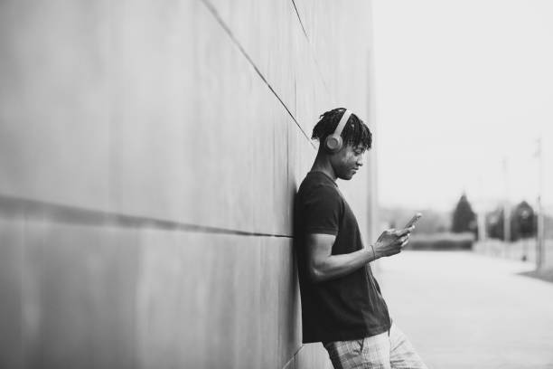 Young adult with headphones listening to music with smartphone, standing on a wall with copy-space. stock photo