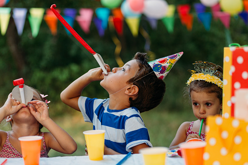 Group of children sitting at the table outdoors and celebrate birthday party