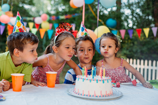 Little girl blowing birthday candles on a outdoors birthday party in the yard