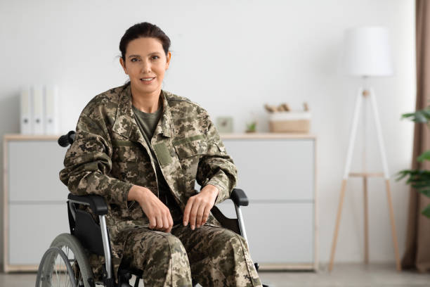 Portrait Of Smiling Female Soldier In Camouflage Uniform Sitting In Wheelchair Indoors Portrait Of Smiling Female Soldier In Camouflage Uniform Sitting In Wheelchair Indoors, Military Woman With Disability Looking At Camera, Enjoying Rehabilitation Process After Trauma, Copy Space female combat soldier stock pictures, royalty-free photos & images