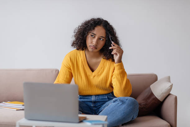 istock Thoughtful young black woman sitting on couch, using laptop computer for online work or studies at home 1479794361