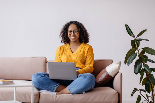 istock Happy millennial black woman in glasses using laptop computer, sitting on couch at home, copy space 1479794552
