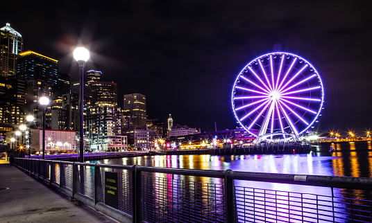The Seattle Great Wheel Lit Up at Night, Reflecting on Pier 69 Harbor in Pacific Ocean, Seattle Washington City Skyline in background, Long Exposure Photography at Nighttime