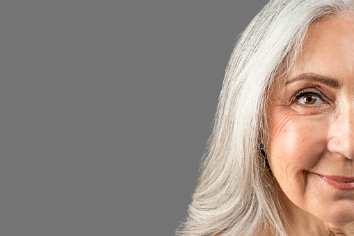 Smiling elderly european woman after anti-aging treatment look at camera, isolated on gray background, studio, close up. Anti wrinkles skin care, beauty procedures, ad and offer, result before, after