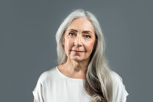 Smiling old european female with gray hair looking at camera, isolated on gray background, studio, empty space. Wrinkle treatment, skin and beauty care, cosmetology, anti-aging procedure, ad and offer