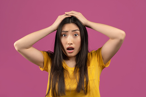 Unbelievable news. Shocked asian woman touching her head, posing over violet studio background. Amazed lady cannot believe amazing offer or sale, opening her mouth in surprise