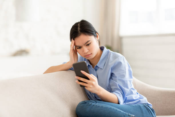 istock Concentrated asian woman sitting on couch, using cell phone 1479795578