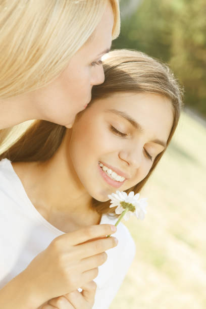 Mother kisses daughter. Close up portrait of mom kissing her daughter holding and smelling a flower