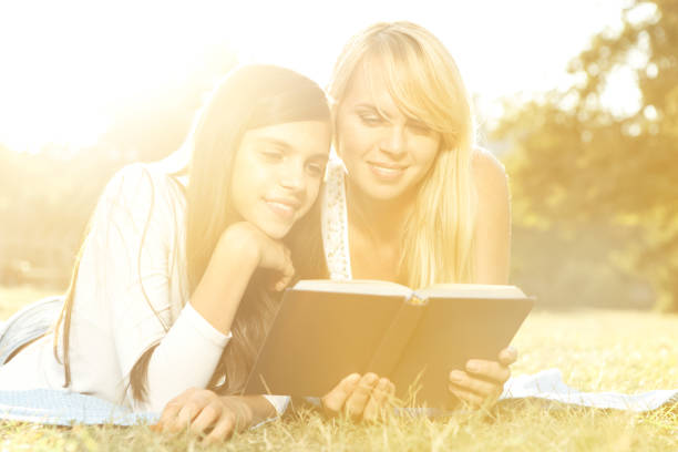 istock Mother and daughter reading book, while lying on sunlit meadow 1479796593