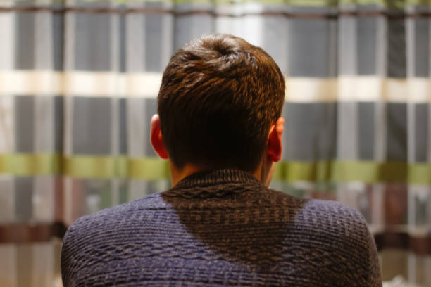 Back view of young man sitting home and thinking. Lost in thoughts, thinking about problem solving, feeling lonely, making important decision, psychological problem. Mental health. Out of focus.