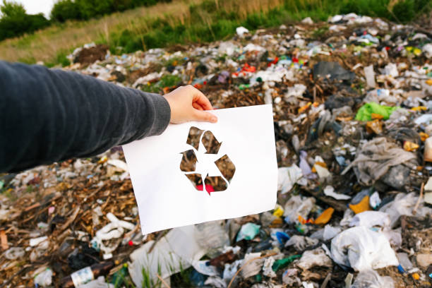 istock Garbage pollution. Hand holding cut paper with the logo of recycling on dump garbage trash background. Recycling concept. Pollution of the planet. Out of focus 1479796779