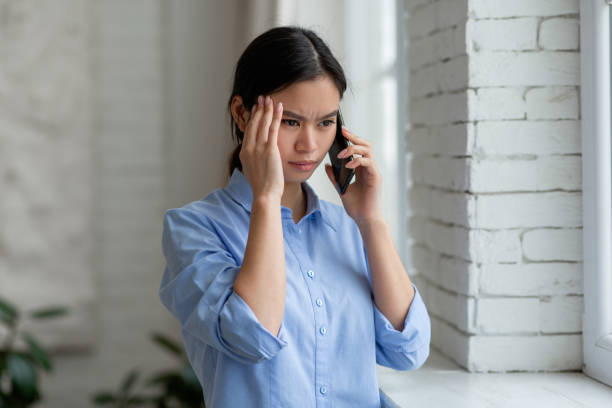 istock Upset asian woman standing by window, having phone conversation 1479797188