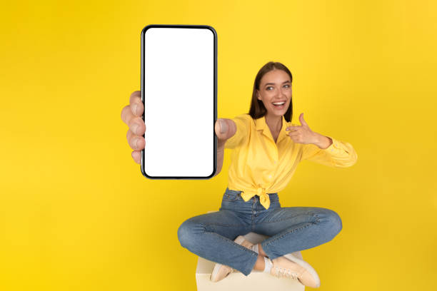 istock Woman Showing Big Smartphone Empty Screen Sitting Over Yellow Background 1479797336